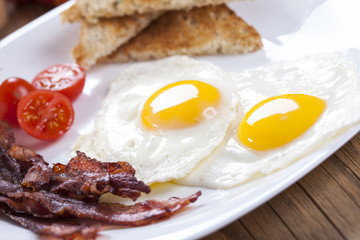 Delicious fried egg with spices, bacon, croutons and tomatoes on