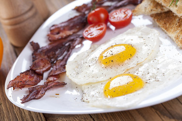 Delicious fried egg with spices, bacon, croutons and tomatoes on