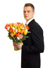 Young man in suit with big bouquet of tulips on white background