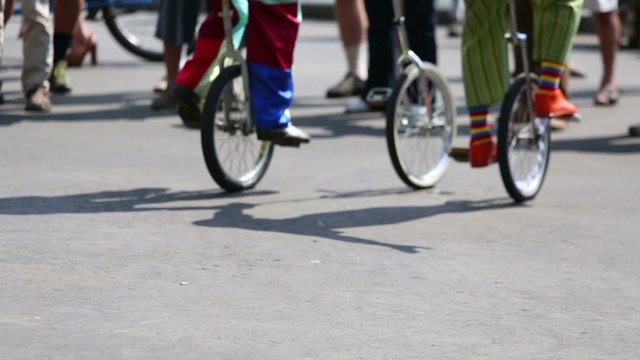 Feet of clowns in colored clothes riding on unicycles outdoor