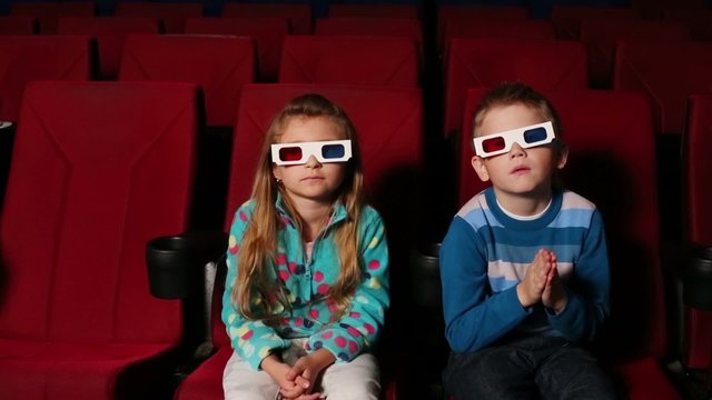 Little boy and girl in 3D glasses sit and watching a movie