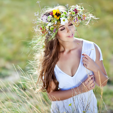 Beautiful woman in a summer field with flower wreath