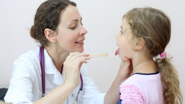 woman doctor in office looks throat to little girl-patient