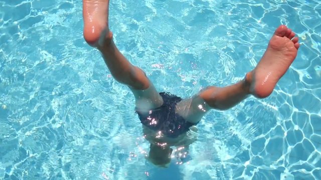 Boy have fun in pool touching pool bottom by hands with feet out