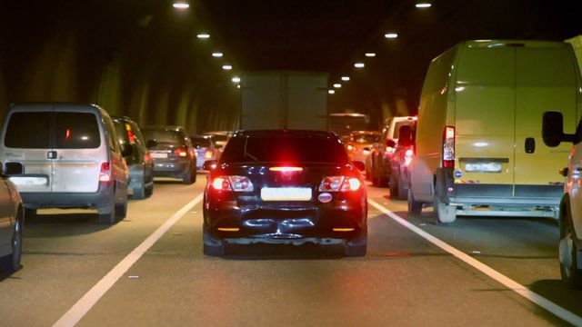 Lot of cars make jam in dark tunnel with illumination, view from car in motion