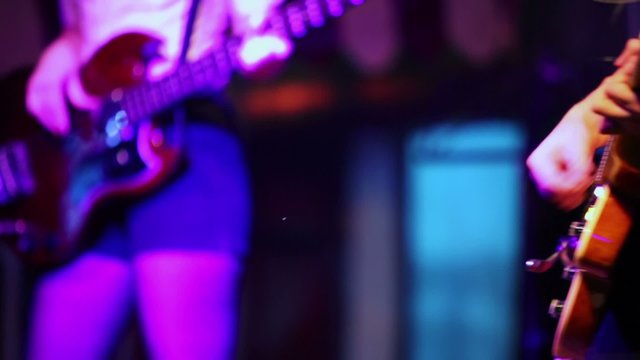 Young man and woman play on guitars on stage during concert