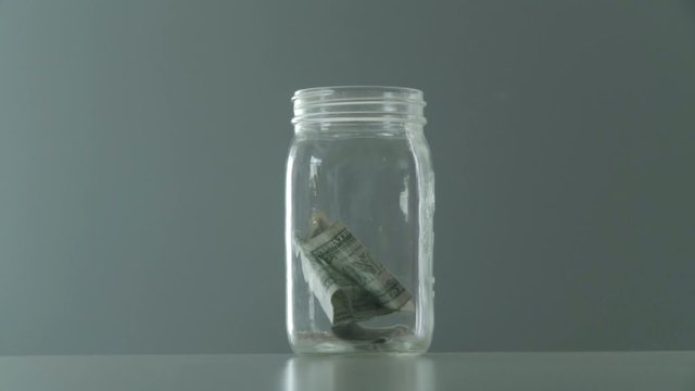 Jar gets filled with one dollar and five dollar bills.  Clip starts at normal speed then gets faster.