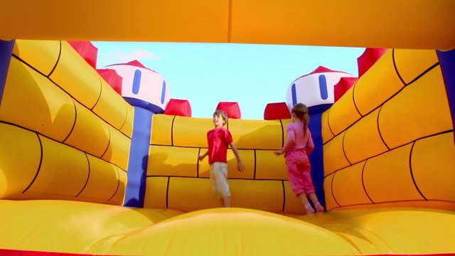 Two kids boy and little girl jump at inflatable playground at sunny summer day
