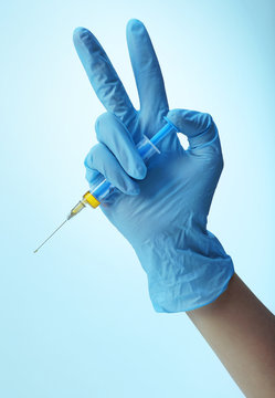 Hand in gloves with syringe on blue background