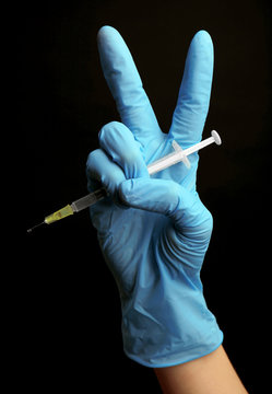 Hands in gloves with syringe on black background