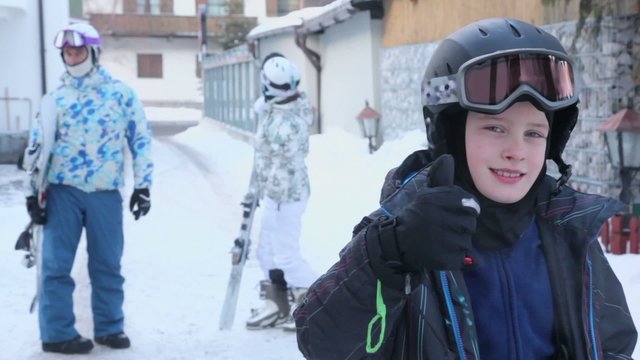 Boy in uniform shows thumb up and parents stand with snowboards