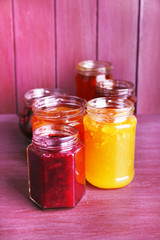 Fototapeta na wymiar Homemade jars of fruits jam on color wooden background