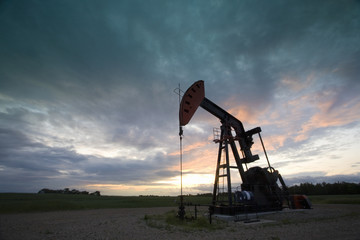 An oil derrick, a well head pump arm with frame, silhouetted against the evening sky. Oil business. 