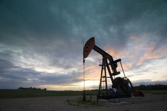 An oil derrick, a well head pump arm with frame, silhouetted against the evening sky. Oil business. 