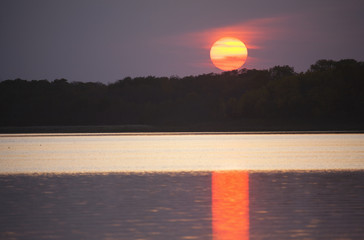 An orange setting sun casting light onto the surface of a lake. 