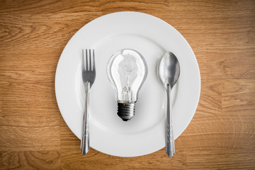 Light bulb in plate and fork and spoon on wooden table