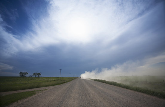 A truck raising dust as it rolls down a prairie road.