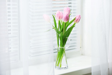 Beautiful pink tulips in glass vase on windowsill background