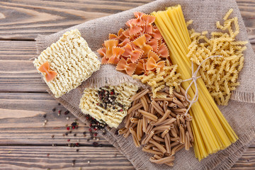 Different types of pasta on sackcloth on wooden background