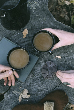 Couple's hands and two mugs of coffee on tree trunk