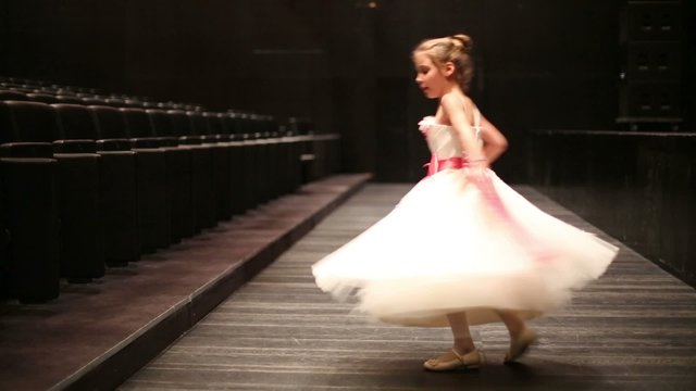 Little girl dressed in puffy gown spins at theatre hall.