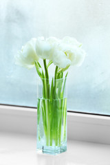 Beautiful white tulips in glass vase on windowsill background