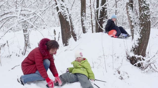 Mother helps daughter after falls, meanwhile son sits on sled
