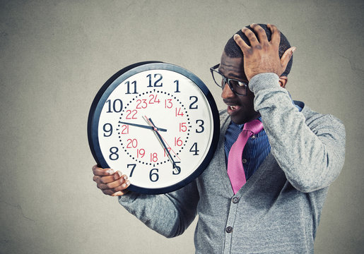 Stressed young man running out of time looking at wall clock