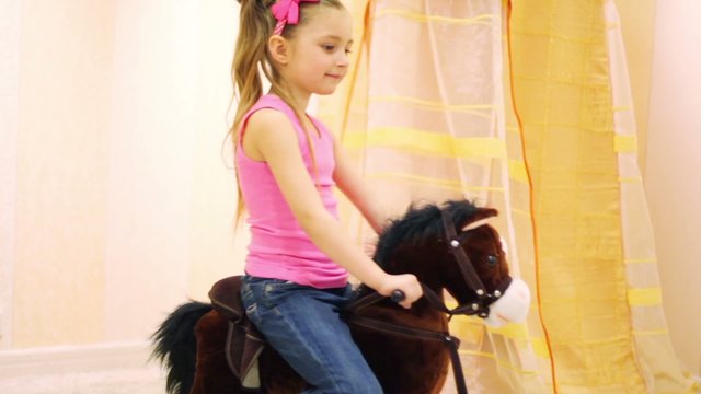 Girl in jeans and t-shirt swinging on brown rocking horse