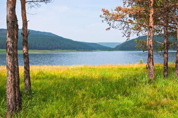 Panele Szklane Podświetlane  Słoneczna łąka z widokiem na jezioro i góry