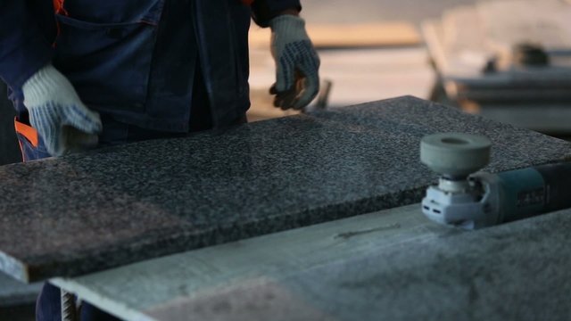 Worker in gloves grinds black marble tiles at construction