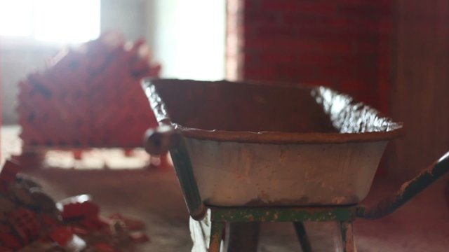 Dirty barrow stand near stack of red bricks at construction site