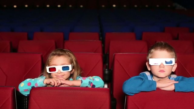 Little boy and girl in glasses watching funny movie in 3D cinema