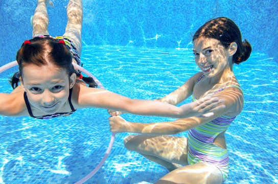Happy children swim in pool underwater, girls swimming