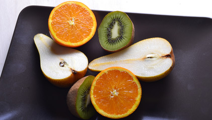 Oranges, kiwi, pears cut on a plate dark color.