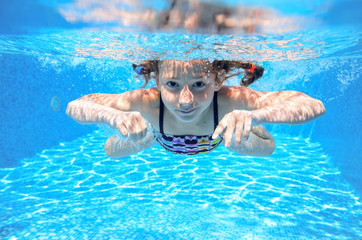 Happy girl swims in pool underwater, active kid swimming