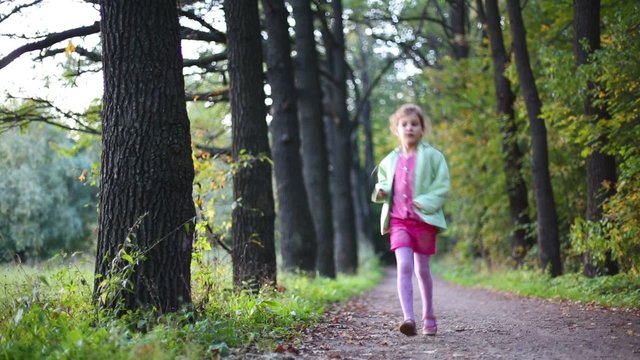 Cute little girl is running on footpath through the forest 