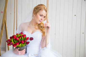 Bride on swing holding her red tulip bouquet