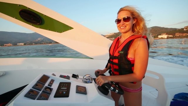Happy dancing woman in lifejacket sails boat on sea at evening