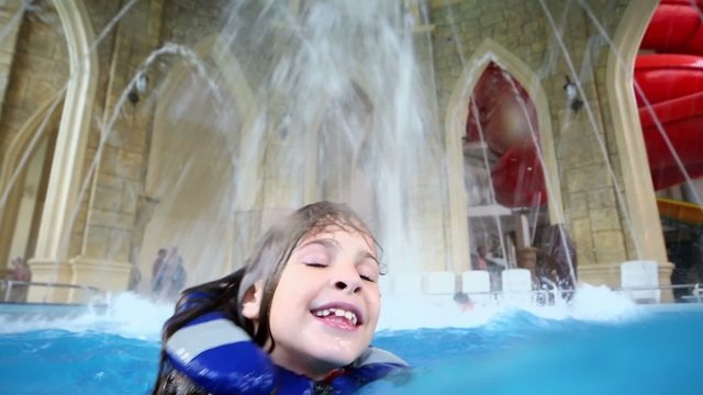 Happy girl in lifejacket swims in pool with jets at water park