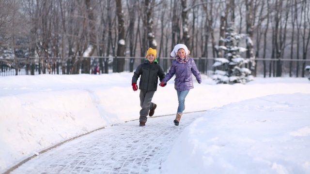 Happy boy and girl run on pathway in park at winter day