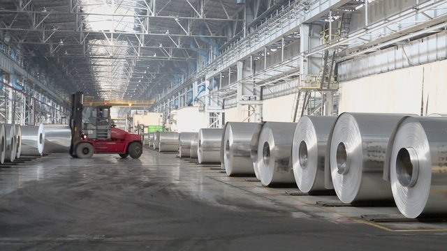 Man in loader machine transports rolls of aluminum at workshop