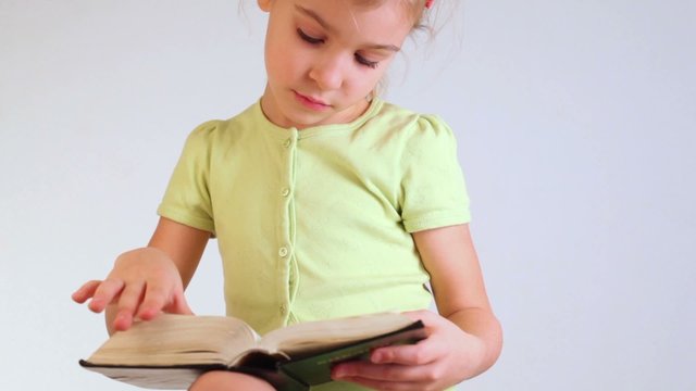 little girl in a green blouse reads book and inverts pages