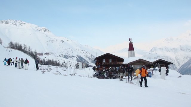 People ride ski and snowboards near rest house with benches