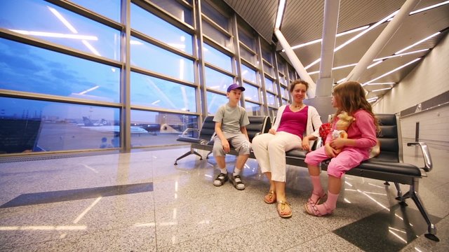 Mother, son and daughter sit in waiting hall of airport and talk