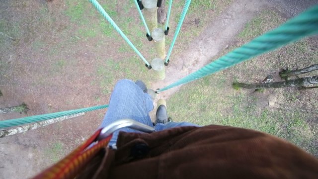Feet of man in jeans on rope way above high trees in park 
