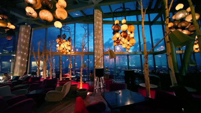 Several people sit in cafe with cityscape view at evening