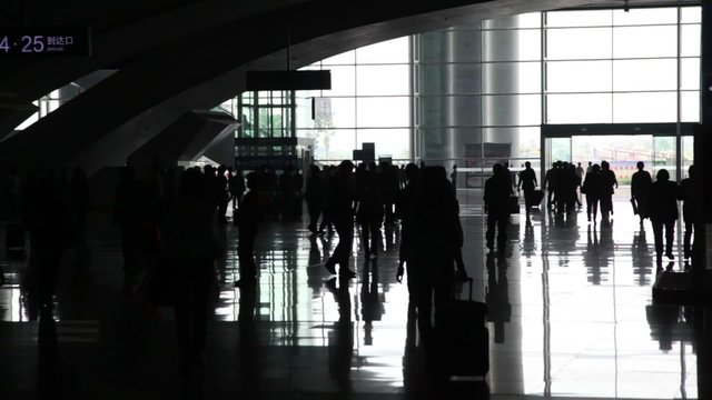 Silhouettes of people with suitcases hurrying in railway station