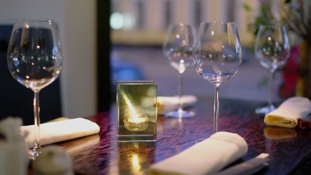 Evening street traffic behind window of restaurant where candle burns at table with glasses and chopsticks