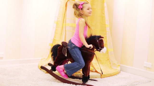 girl swinging on rocking horse and pinch it by hitting rump